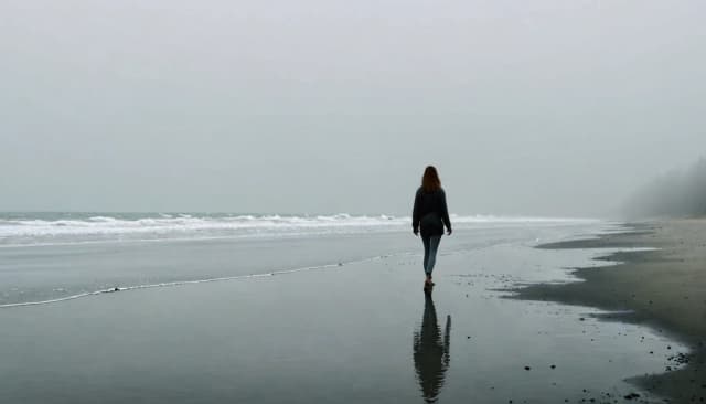 Берег океана. Мужчина идет вдоль кромки воды. Серое небо, туман. В небе проявляется лицо красивой девушки.