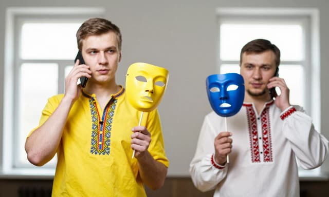 A 25-year-old man in a yellow national Ukrainian shirt with blue embroidery is talking on the phone, in his other hand is a yellow theatrical mask on a stick, a man in a white Russian national shirt with red embroidery is talking on the phone, in his other hand is a blue theatrical mask on a stick, two windows