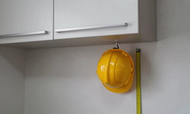 interior photo of a small kitchen with wall-mounted upper cabinets, depth of 35cm, a yellow hard hat hanging from a hook below the cabinet to indicate head clearance issue, measuring scale stuck on cabinet side, tight workspace below, no people, no hands, no text on image, realistic overcast lighting, 8k --ar 16:9 --style raw