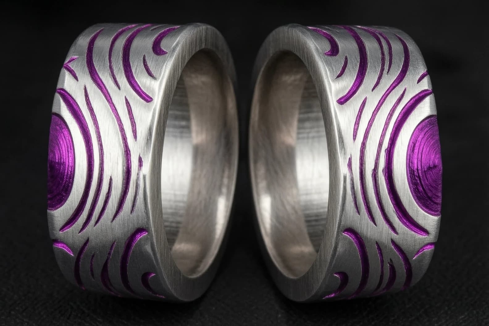 Use the attached reference image as the exact source design. Split the ring shown in the image horizontally along its width (parallel to the band’s plane), not vertically. The cut should go through the middle of the ring’s thickness, creating two halves that stack together to form the original ring. Preserve all details exactly: brushed silver texture, vivid purple-magenta inlays, swirling patterns, central circular motif, and crescent elements. Show the two halves side by side, with the cut surfaces facing the viewer to clearly demonstrate the horizontal split. Treat the two halves as a matching set; they must look like complementary parts of one original ring from the reference image. Explicitly avoid vertical splitting; the cut must be horizontal through the ring’s thickness. Use the attached image as the only design source — do not alter patterns or colors