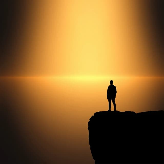 A lone human silhouette standing at the edge of a cliff, seen from behind, looking out at a vast open horizon. The figure is free, calm, at peace. Ahead: warm dawn light breaking through, golden and soft. Behind: darkness fading into shadow. No chains, no cage, no walls. Just open space. The figure is not running. Not escaping. Just standing. Just breathing. Just being. Cinematic lighting, dramatic contrast, deep blacks giving way to warm golds. Photorealistic, minimal, emotional, symbolic. Vertical composition. No text. Mood: freedom, peace, the first breath after a long suffocation