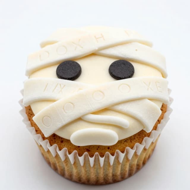 A cupcake in the form of a mummy's face, with bandages located along the entire key from the top edge to the bottom edge. At the same time, the bandages are engraved on it.